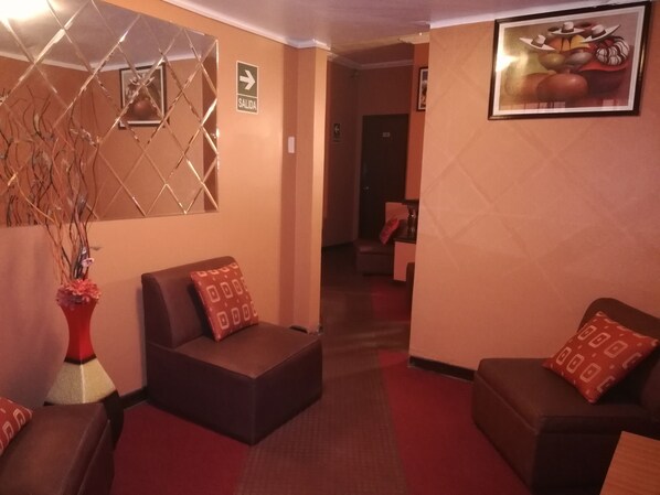 A lobby with a red carpet, two brown sofas with patterned cushions, a decorative wall piece, and a framed picture.