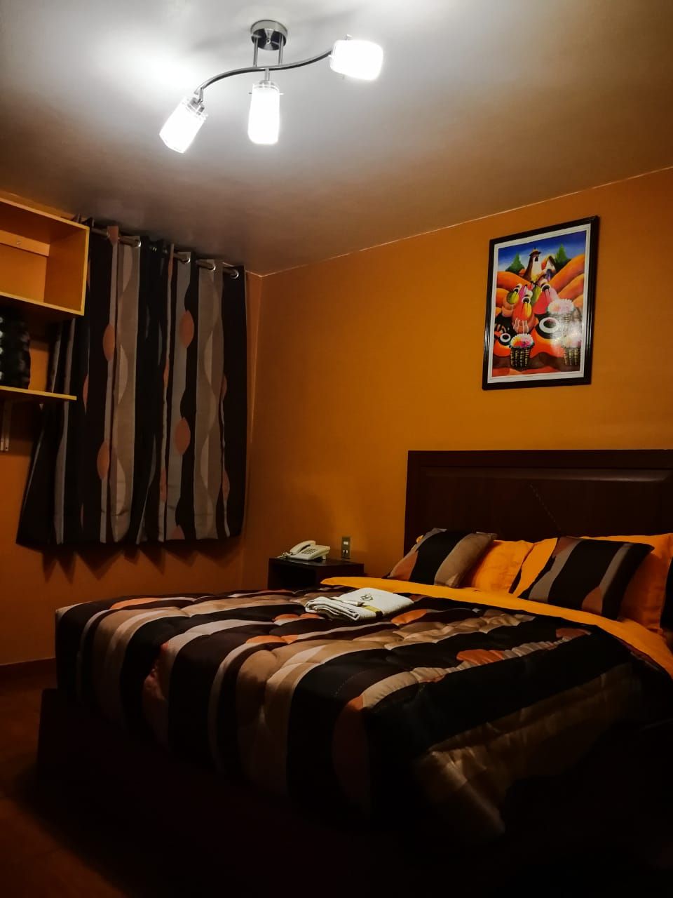 Una habitación de hotel con una cama, una mesita de noche, un teléfono y un cuadro en la pared.
