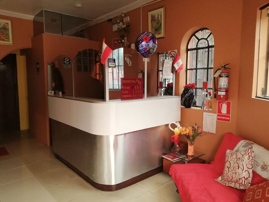 Un área de recepción con mostrador, un sofá rojo, un jarrón con flores y un extintor en la pared.