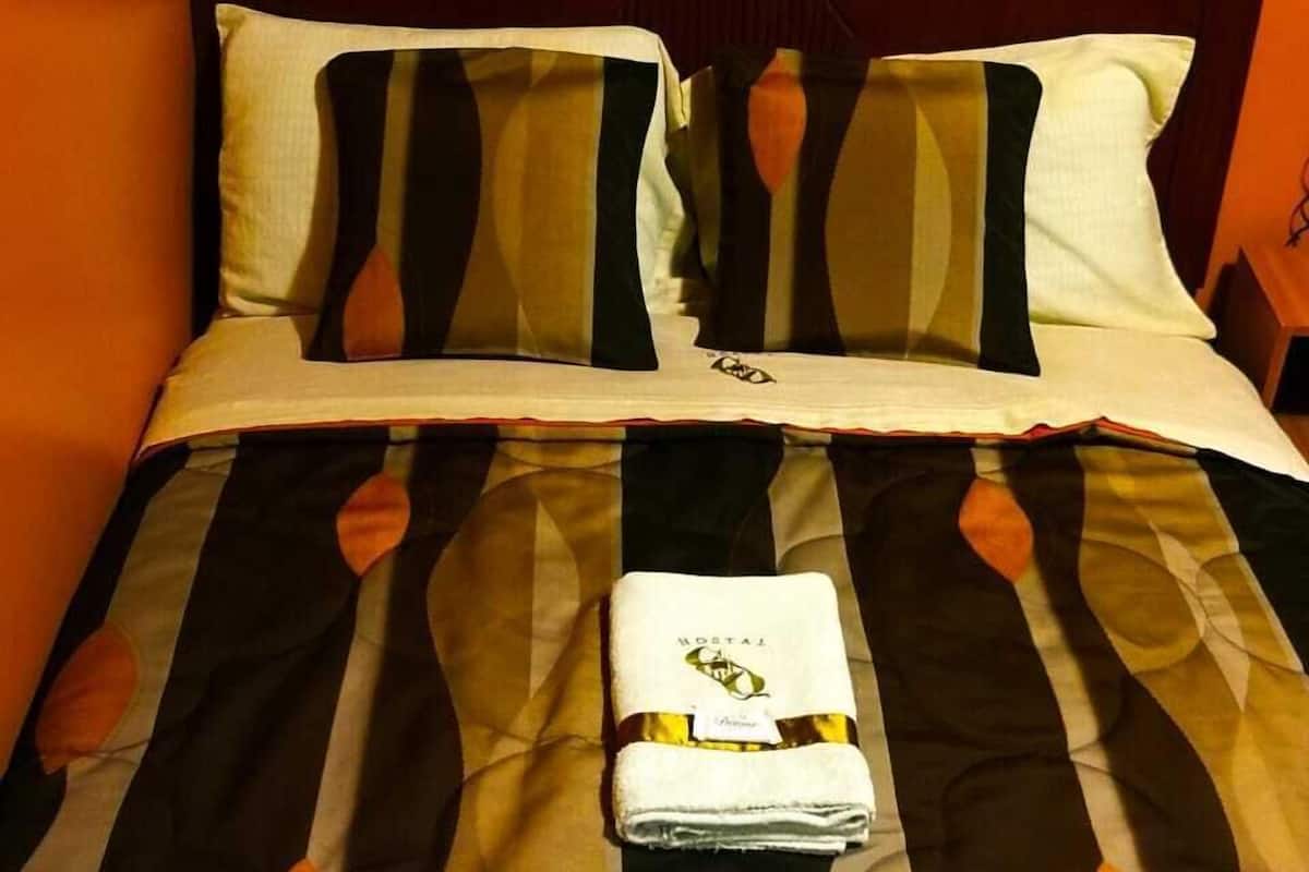A neatly made bed with a patterned bedspread, two pillows, and a folded towel on the bed.