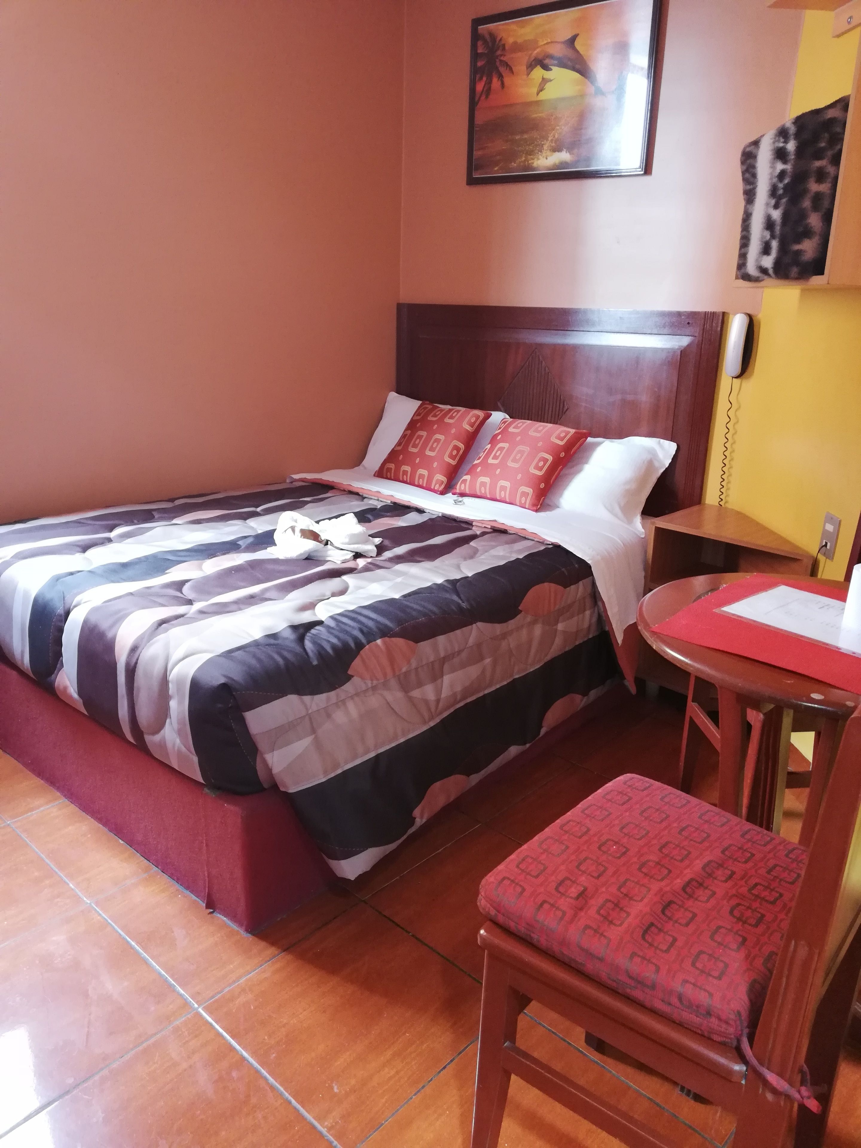 Une chambre d’hôtel avec un lit, une tête de lit en bois, une table de chevet, une table et une chaise.