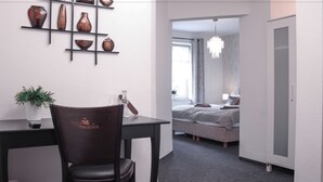 Una habitación de hotel moderna con comedor que presenta una mesa y silla de madera oscura, un conjunto de jarrones en la pared y una cama con cabecera gris y ropa de cama blanca.