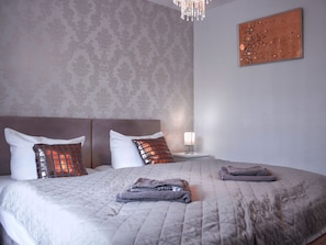 Una cama bien hecha con un edredón gris acolchado, dos almohadas y toallas dobladas a un lado.