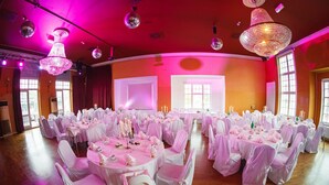 Un gran salón con mesas redondas cubiertas con manteles blancos y sillas, dispuesto para un evento formal.