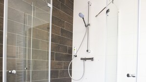 Ducha con paredes de vidrio, piso de baldosas, ducha de pared y ducha de mano.
