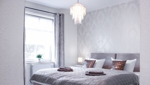 Un dormitorio con una cama grande, una mesita de noche, una lámpara y una ventana con cortinas.
