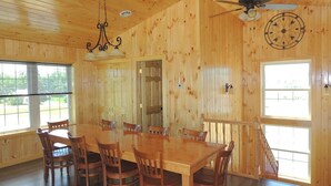A wooden interior with a dining table and chairs, a ceiling fan, and large windows.
