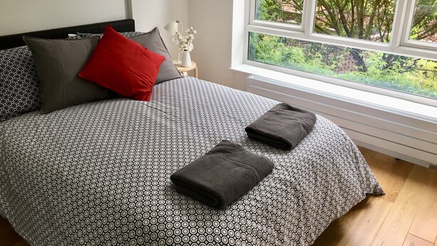 Un lit bien fait, avec une couvre-lit à motifs, deux oreillers et deux serviettes pliées.