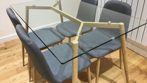 Une table à manger avec un plateau en verre, accompagnée de quatre chaises grises à revêtement rembourré.