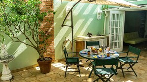 Une terrasse avec une table ronde, des chaises, un pot de fleurs, une petite statue et un mur en briques.
