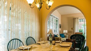 Un coin repas avec une table dressée pour deux personnes, un lustre et une vue sur le salon, accessible par une arche.