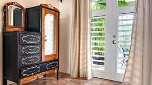 Una habitació amb un armari de fusta negra amb pomes decoratives, un mirall i una porta amb un panell de vidre i plantes verdes.