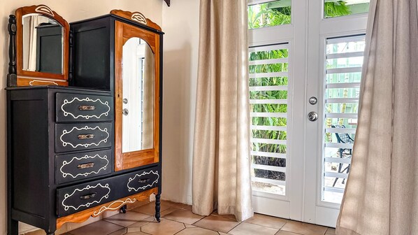 A room with a black wooden dresser with ornate handles, a mirror, and a door with a glass panel and green plants.