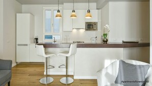 A modern kitchen with white cabinets, a central island with bar stools, pendant lighting, and a microwave. - Apartments Florence - Ponte Vecchio Guelfo (Florence)