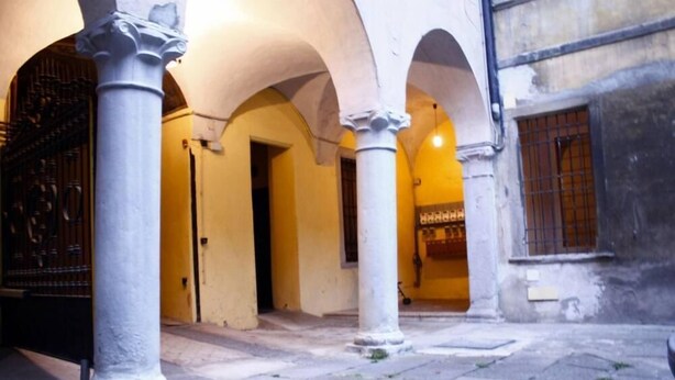 An interior courtyard with arches and columns, a door, and a window with barred shutters. - Bergamo: House with character (Bergamo)