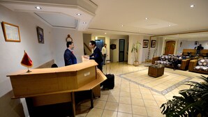 Zona de recepción de hotel con un escritorio de madera, mostrador de recepción y un área de estar con sofás.
