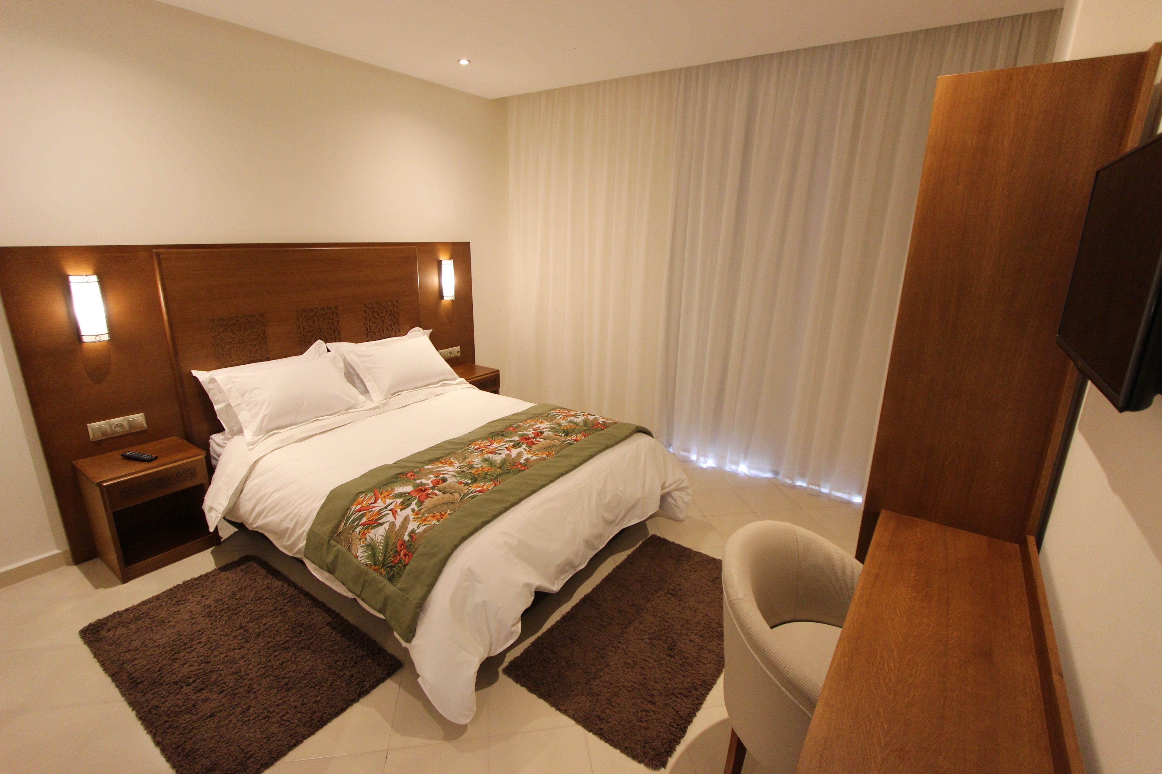 A hotel room with a large bed, a nightstand, a desk, and a TV.