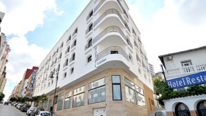 Un hotel blanco con balcones y una entrada en esquina.