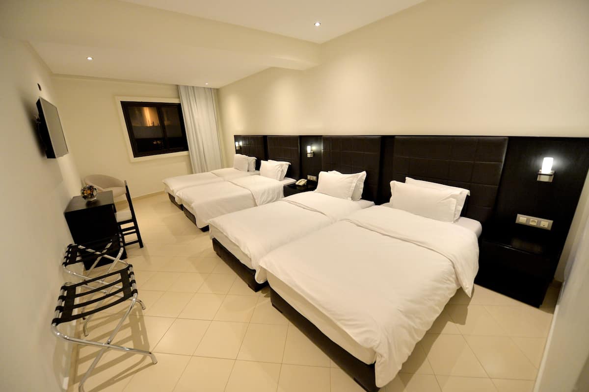 A hotel room with three beds, a desk, a chair, and a TV.