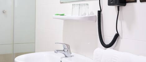A bathroom with a white sink, a glass shower enclosure, a mirror, and a telephone mounted on the wall.