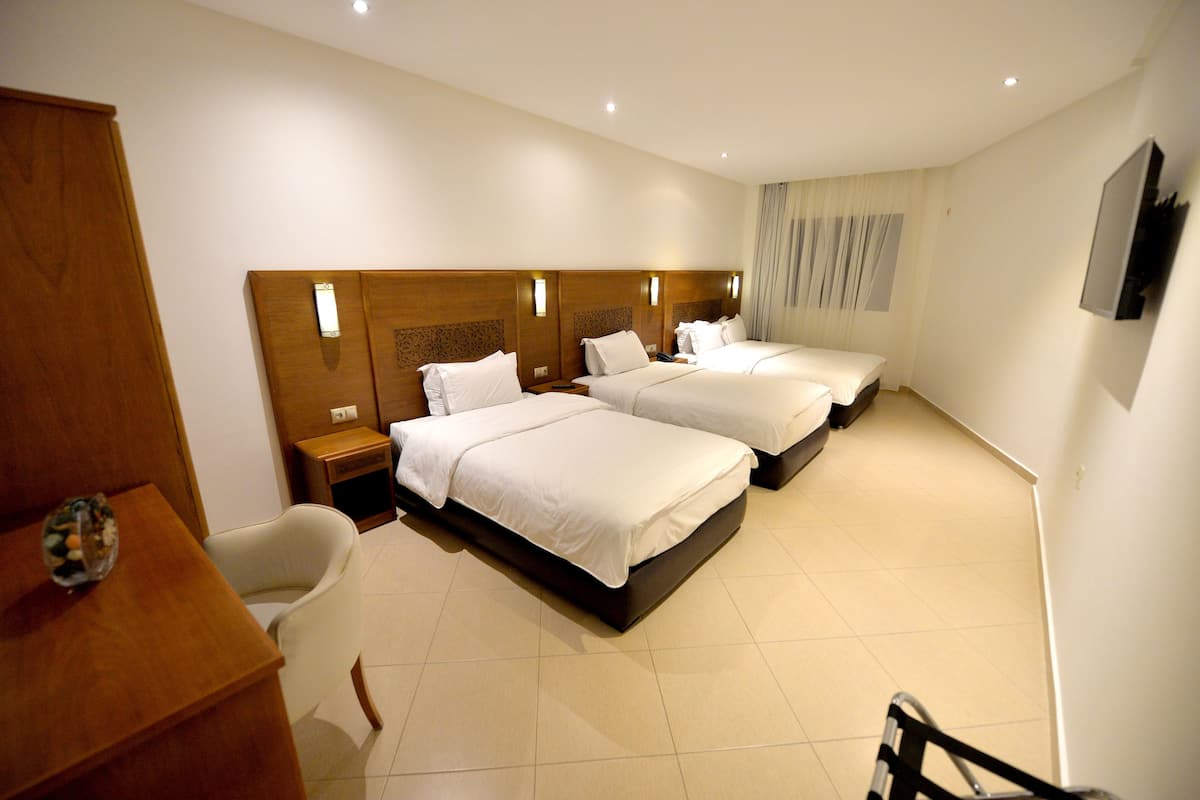 A hotel room with two beds, a wooden headboard, a small table with a vase, and a chair.
