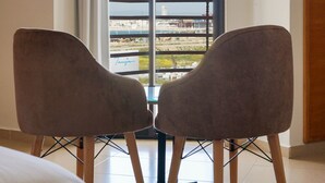 Una habitación con dos sillas orientadas a un ventanal con vistas a una playa y un edificio.