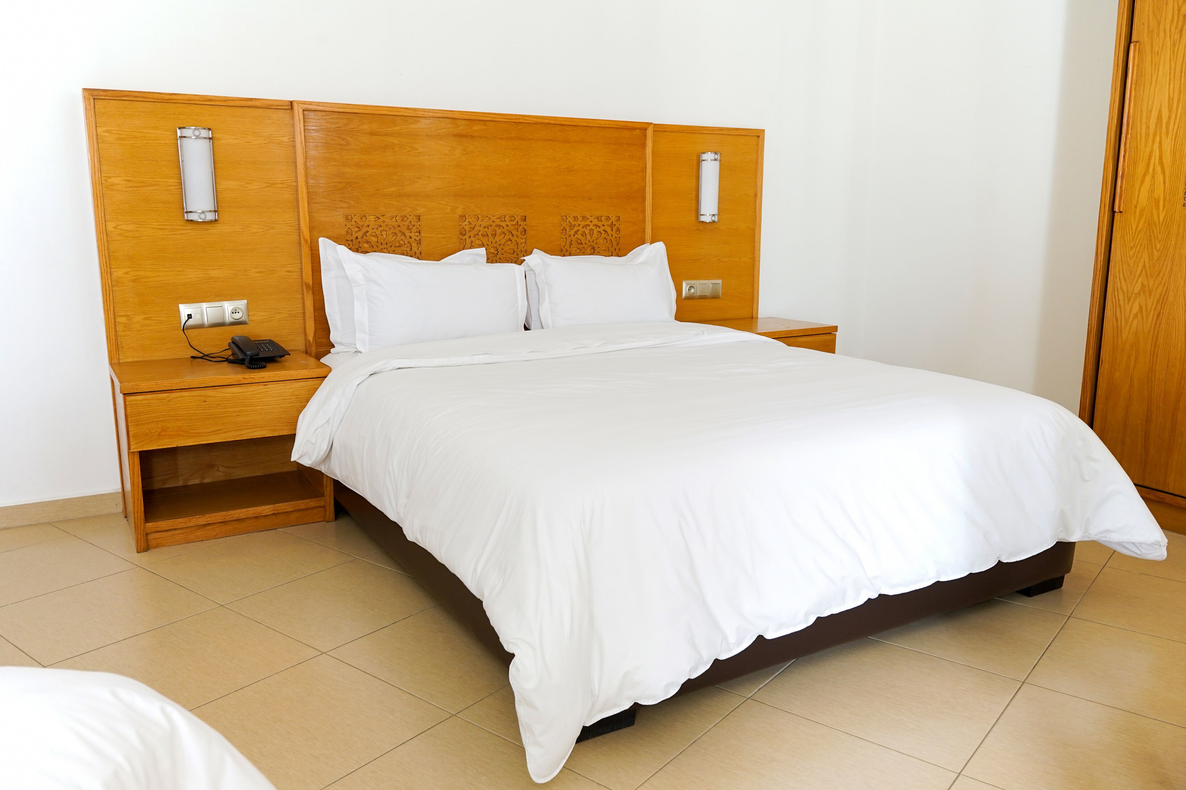 A neatly made bed with a wooden headboard, bedside tables with lamps, and a power outlet on the nightstand.
