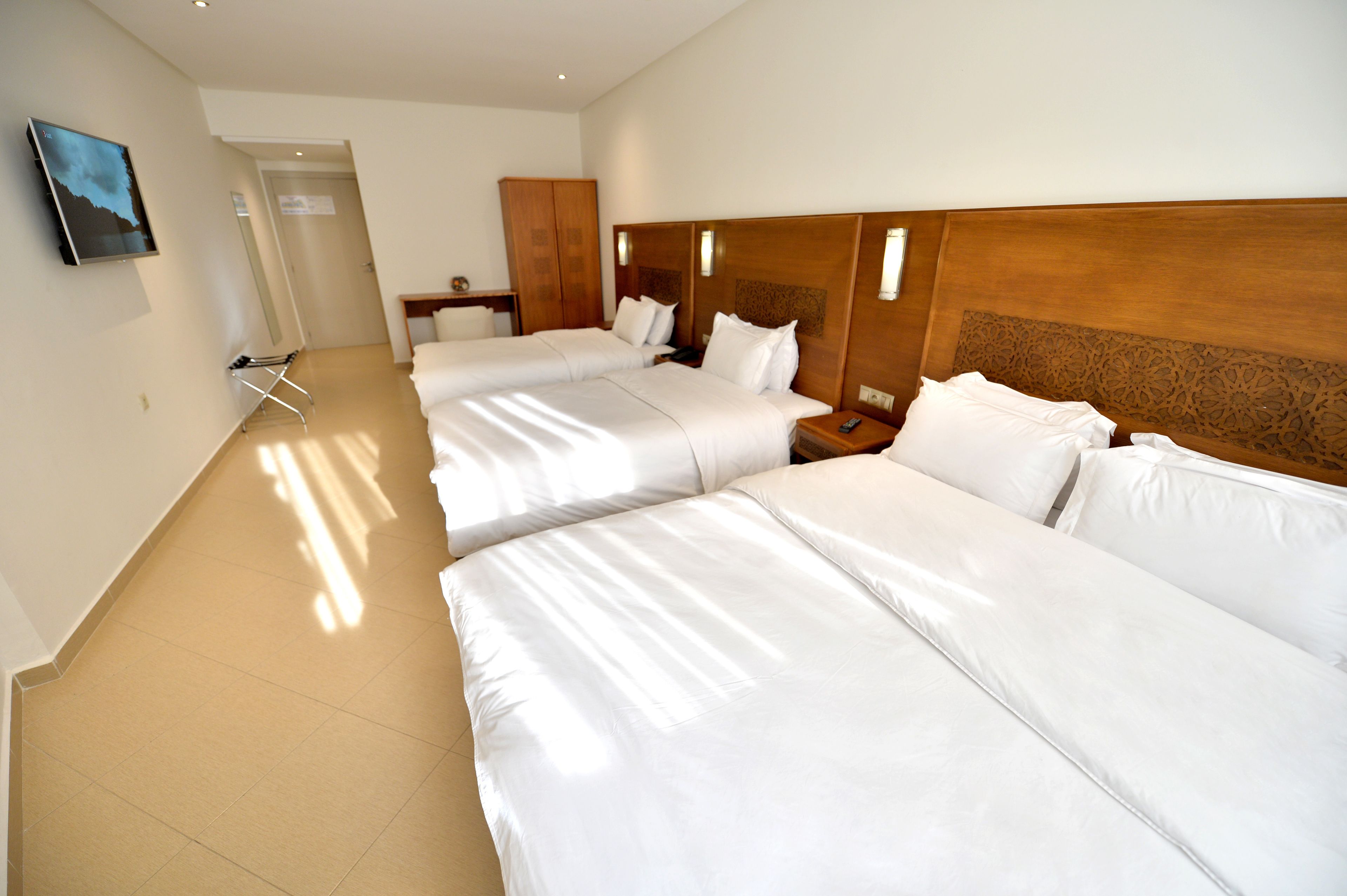 A hotel room with two beds, a wooden headboard, a nightstand, a TV, and a door leading to another room.