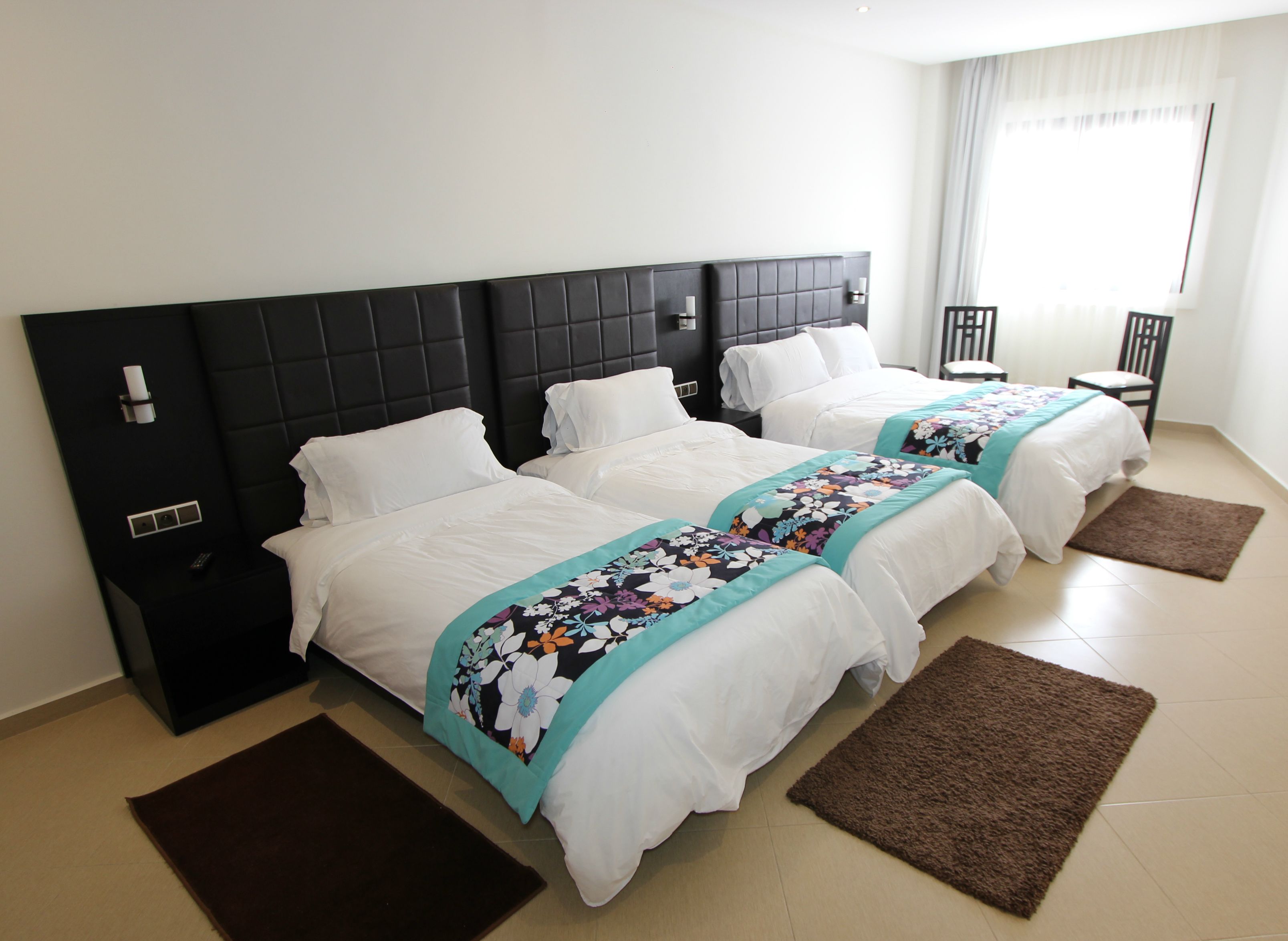A hotel room with three beds, a black headboard, white bedding, and a floral bedspread.