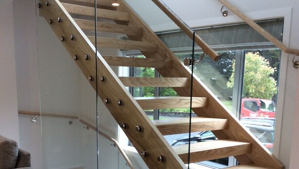 A modern staircase with wooden steps and glass railings, leading to an upper floor.