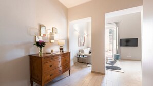 A wooden dresser with drawers, a mirror, and a vase with flowers. There is a small table with a lamp and a television mounted on the wall. - Apartments Florence - Alfani Terrace (Firenze)