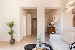 A modern living room with a sofa, a coffee table, a potted plant, and a hallway leading to a kitchen area.