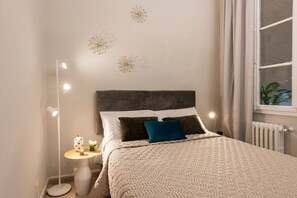 Une chambre à coucher comprenant un lit, une table de chevet, une lampe, des éléments de décoration murale et une fenêtre avec des rideaux.