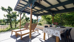 Un patio al aire libre con una mesa y sillas, un banco de madera y una estructura de pérgola.