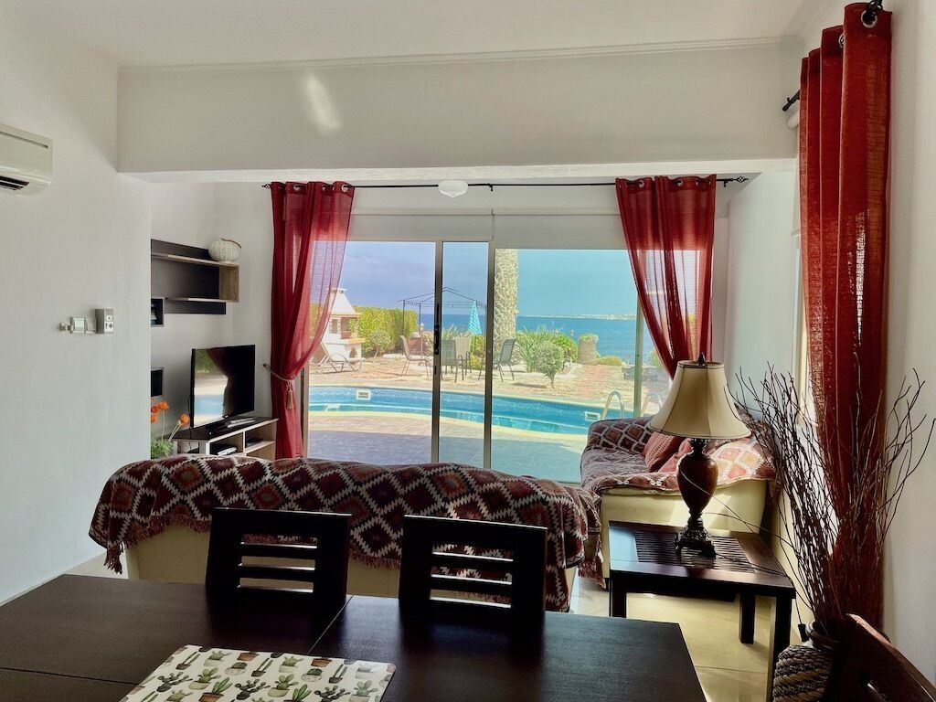 Un dormitorio con un ventanal grande, una cama, un televisor y una zona de comedor con mesa y sillas.