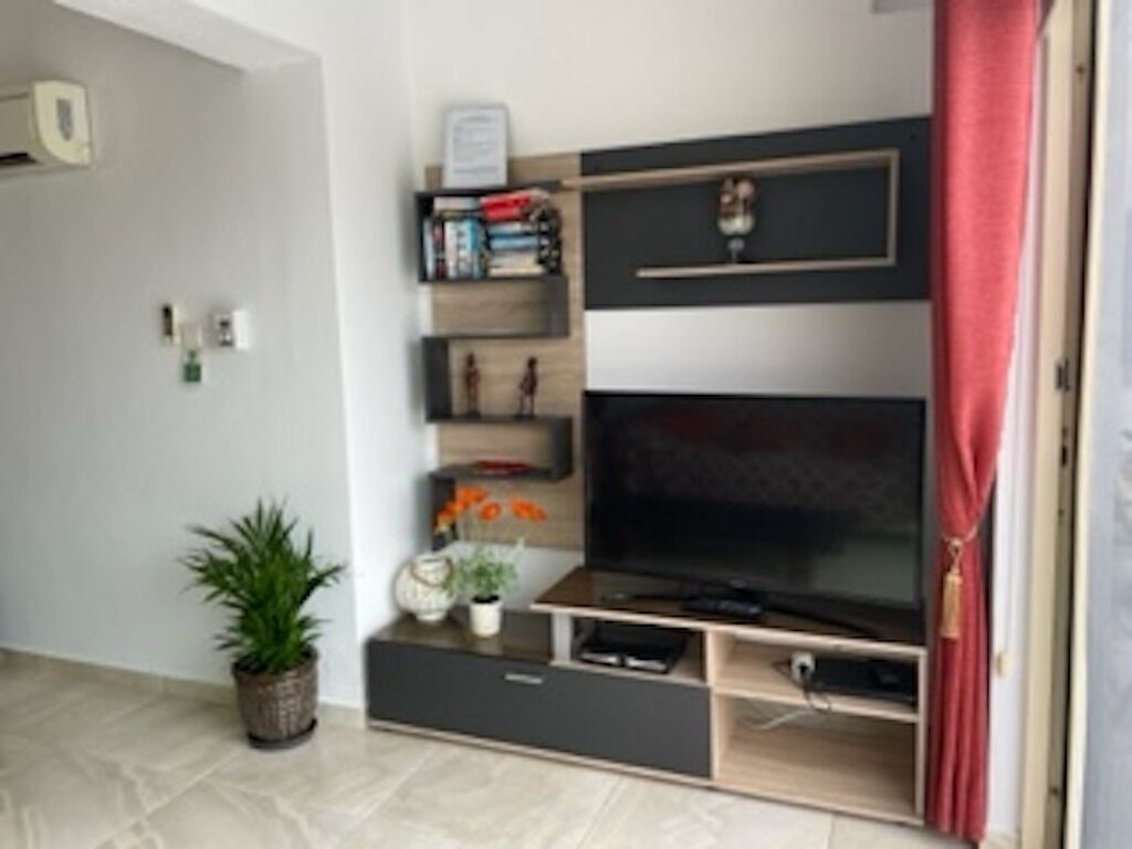 A living room with a flat-screen TV, built-in shelves, a potted plant, and a red curtain.