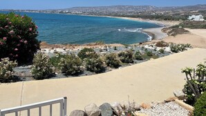 Ett kustlandskap med fri utsikt över havet, en sandstrand och ett belagt område med ett räcke.