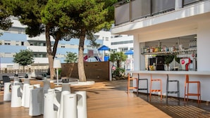 An outdoor bar area with white stools, a bar counter, and a play structure in the background. - HOTEL PLAYASOL MARE NOSTRUM (Ibiza Town)