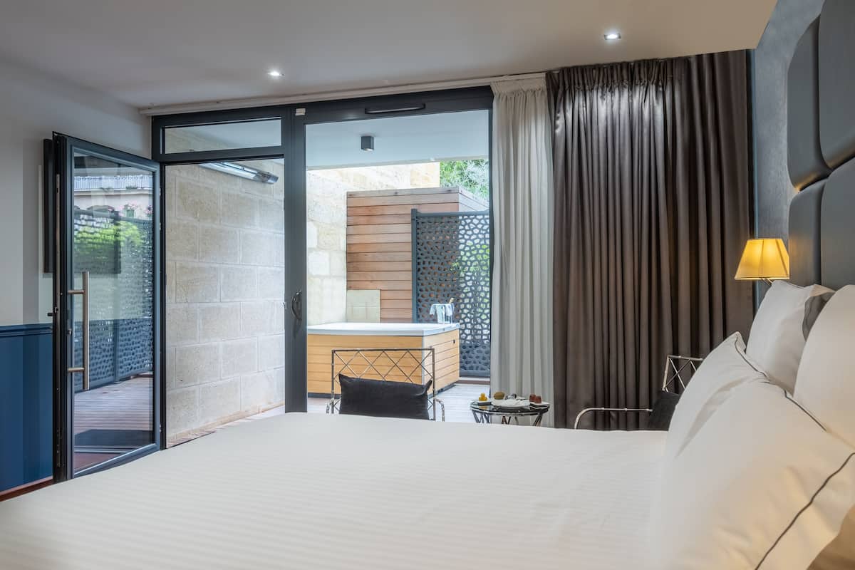Un hotel moderno con una cama grande, un escritorio con silla, una mesita con lámpara y vistas al balcón exterior.