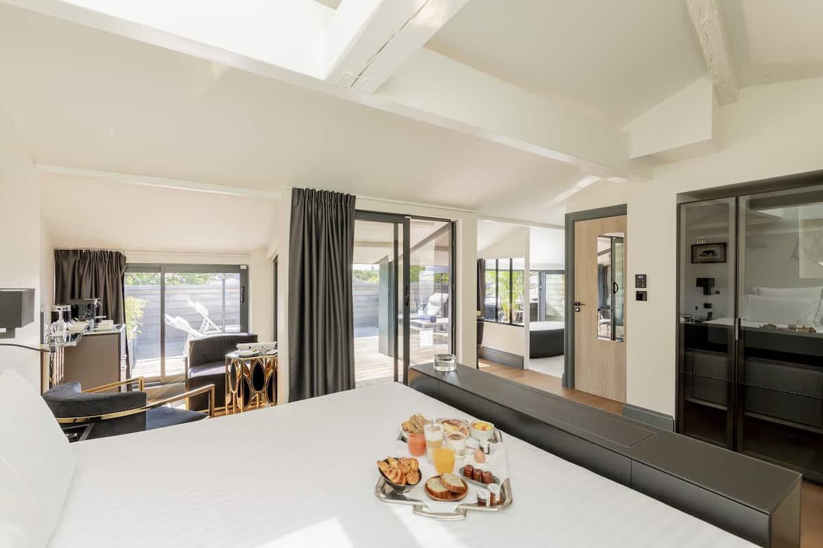 Habitación de hotel con cama, bandeja de desayuno, escritorio con silla, televisor y balcón con mobiliario exterior.