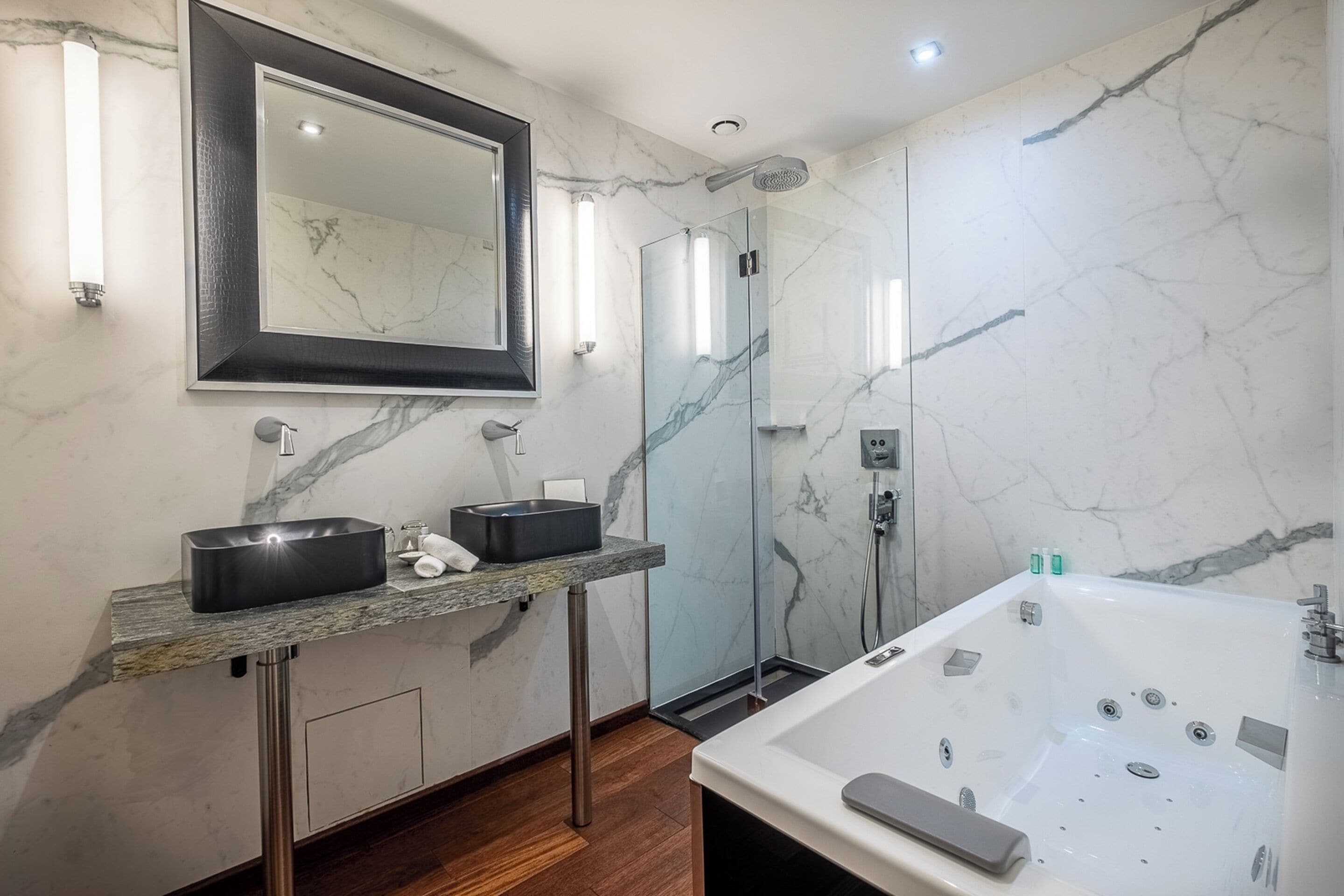 Un baño moderno con un espejo grande, dos lavamanos, una ducha a ras de suelo y una bañera independiente.