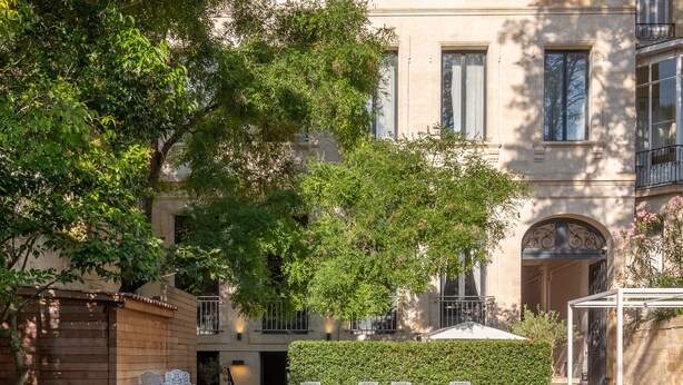 A pool area with a reflection of the building and trees, surrounded by outdoor seating and a well-maintained lawn. - Le Palais Gallien Hôtel & Spa (Bordeaux)