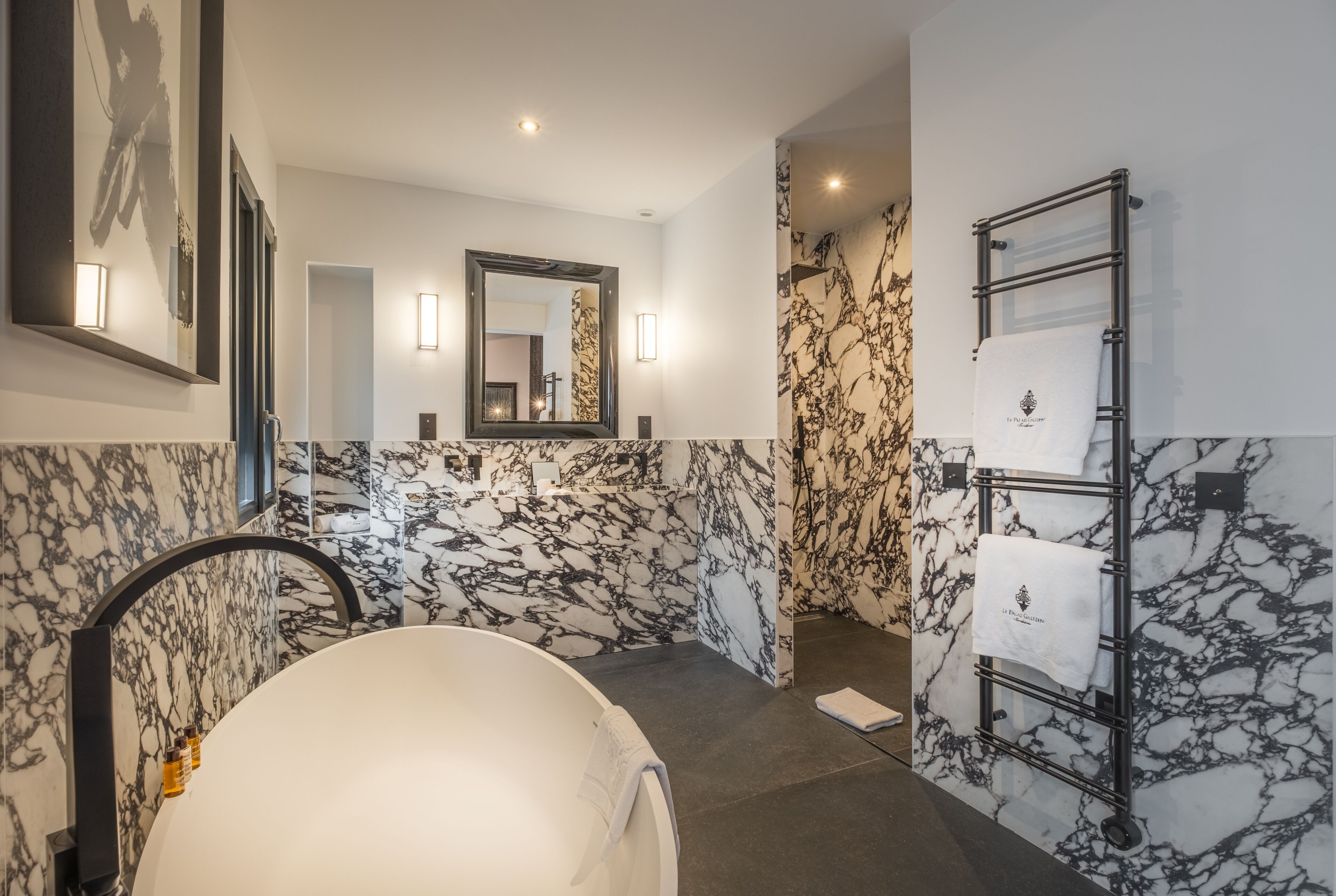 Ein modernes Badezimmer mit einer großzügigen Badewanne, Marmorwänden, einem Spiegel und einem Handtuchhalter.
