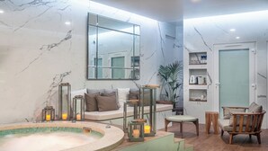 A modern bathroom with a marble wall, a large mirror, a bathtub, and a seating area with a sofa and a chair. - Le Palais Gallien Hôtel & Spa (Bordeaux)