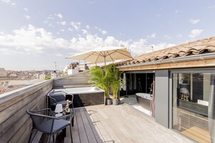 Una terraza en la azotea con cubierta de madera, mobiliario exterior, un paraguas grande y un baño moderno.