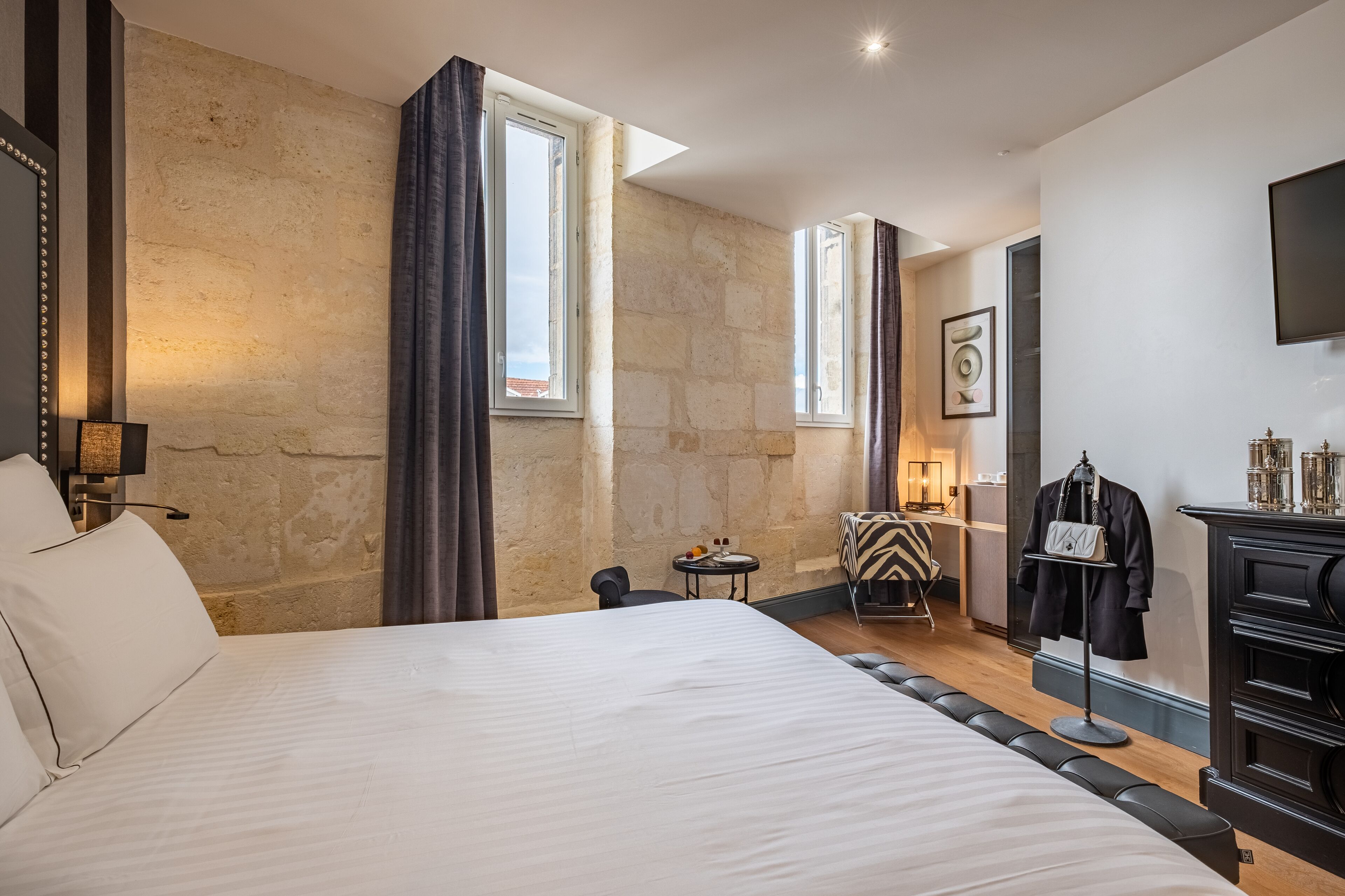 A hotel room with a large bed, a desk, a chair, and a wardrobe.