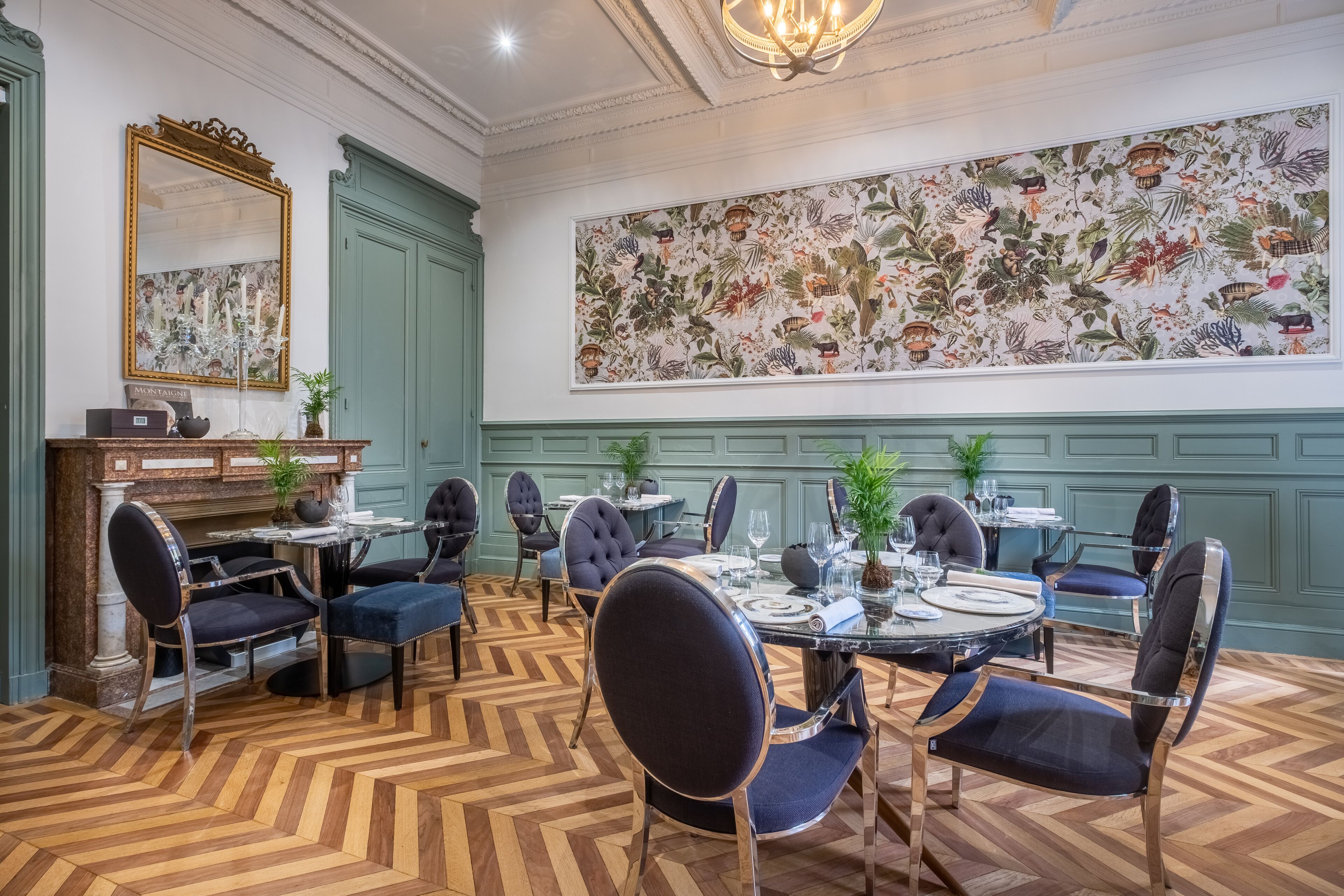 Een eetkamer met een grote bloempracht muurschildering, groene lambrisering en een visgraatvloer.