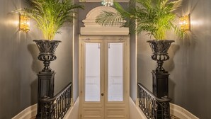 A grand hallway with a chandelier, two potted plants, a double door, and a patterned carpet. - Le Palais Gallien Hôtel & Spa (Bordeaux)