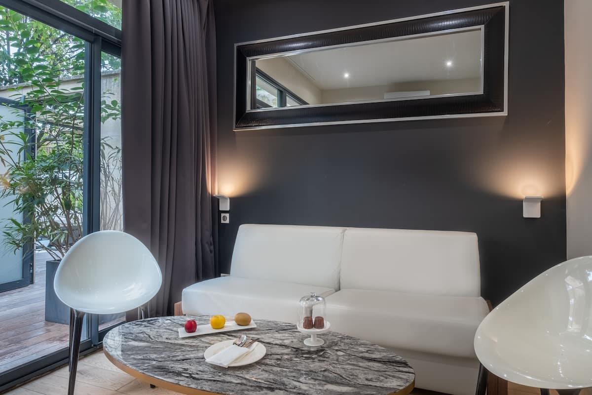 Una habitación moderna con un sofá blanco, una mesa redonda de mármol y un centro de mesa con una cúpula de cristal, además de un espejo grande en la pared.