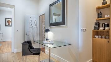 A modern room with a glass table, a black chair, a mirror, and a wooden cabinet with shelves.